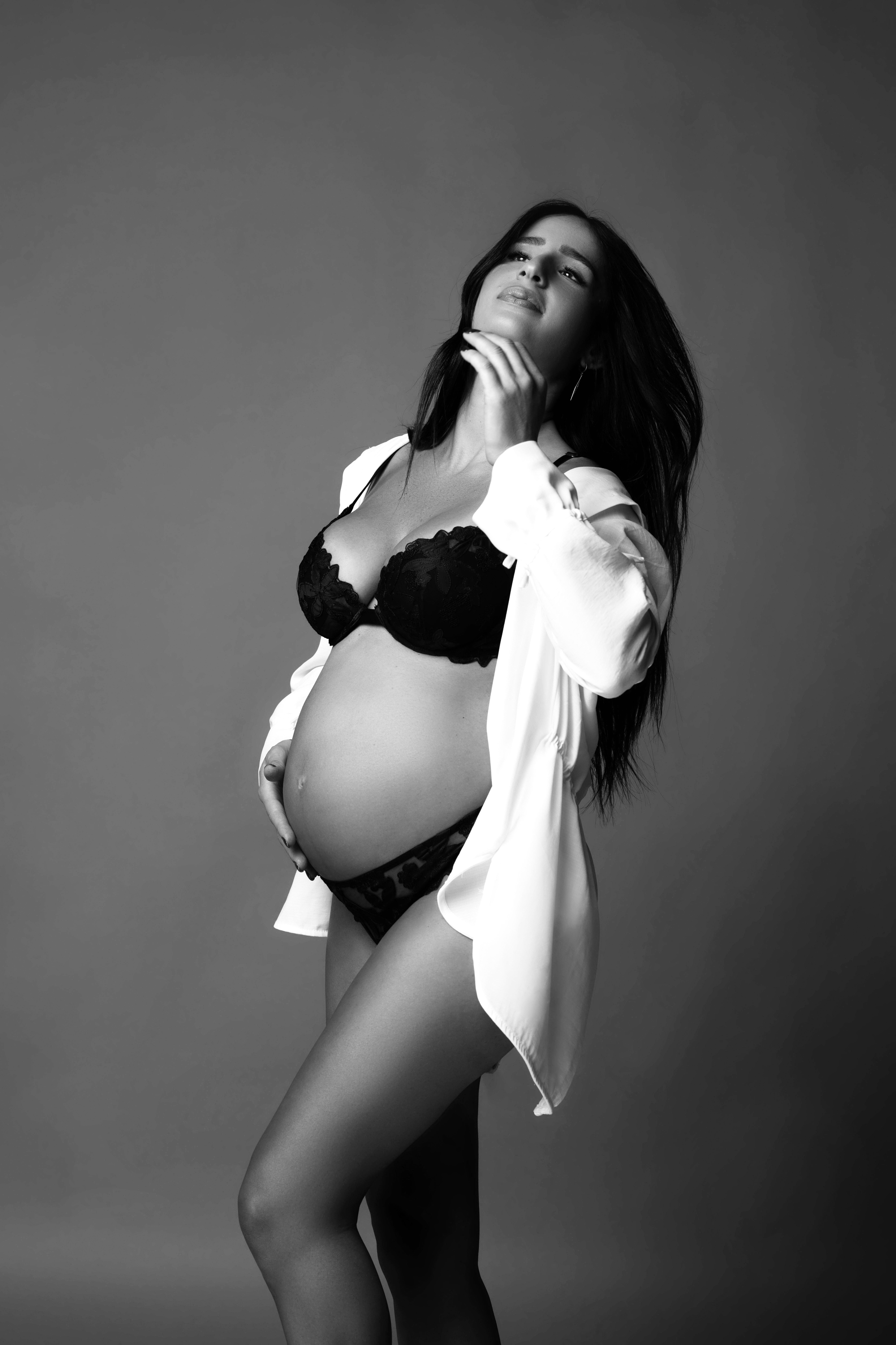 Pregnant woman in black bikini wearing open white button-down shirt